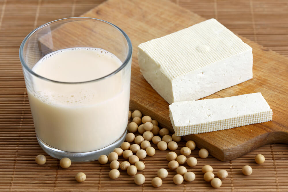  Verre de lait de soja avec de la mousse sur un tapis de bambou avec des fèves de soja - Mousse de lait de soja
