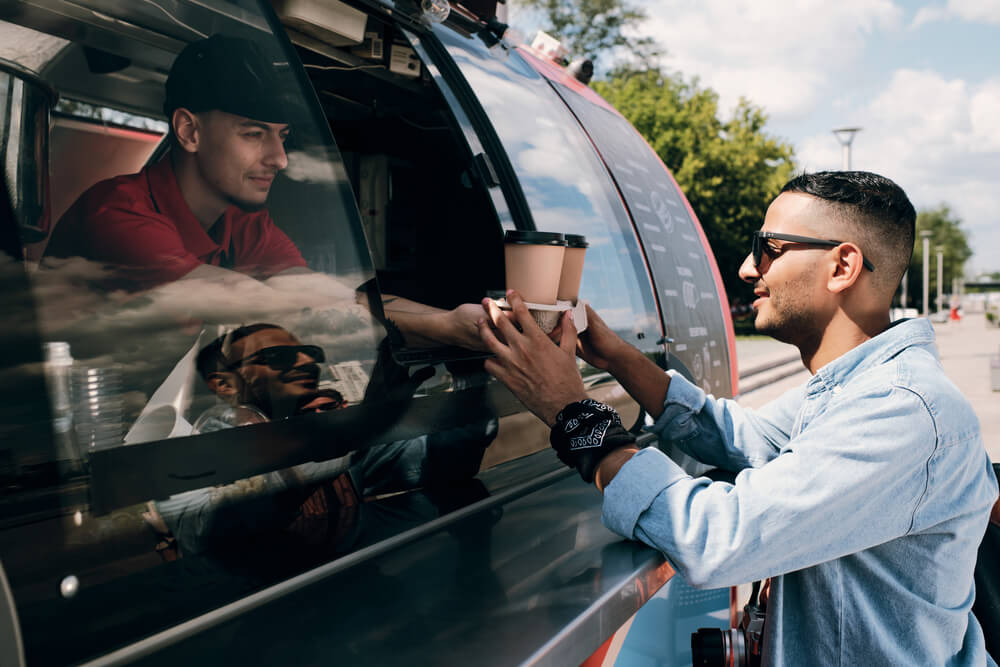 Guy in casualwear and sunglasses buying two drinks in food truck
