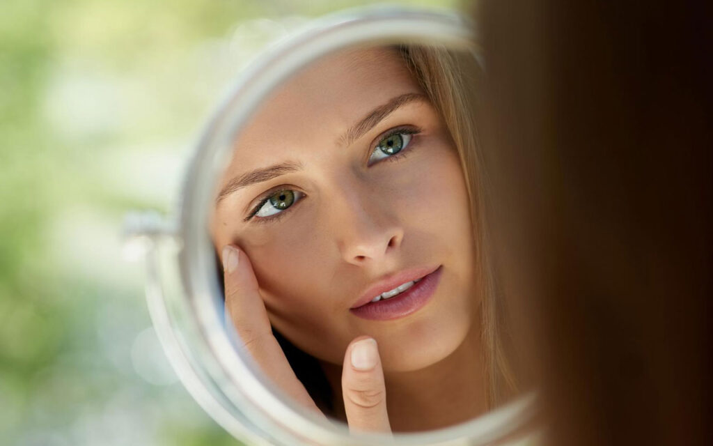an attractive young woman touching her skin in front of the mirror