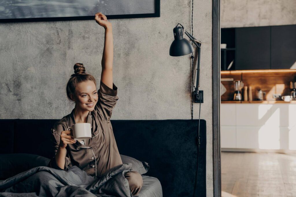 Attractive young happy female having morning coffee in bed