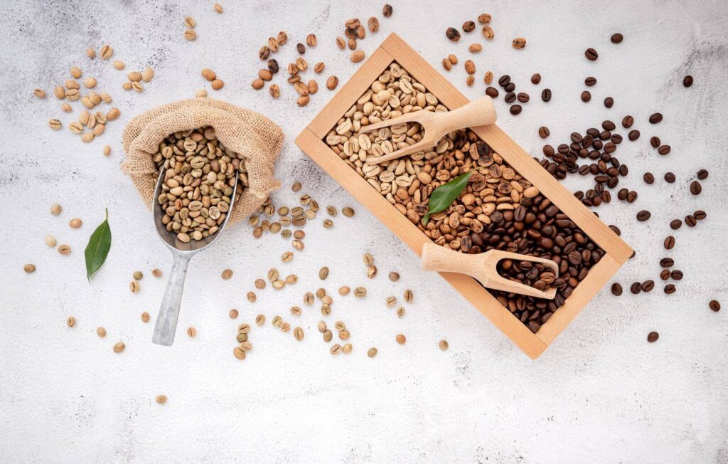 Green and brown decaf unroasted and dark roasted coffee beans in a wooden box with scoops