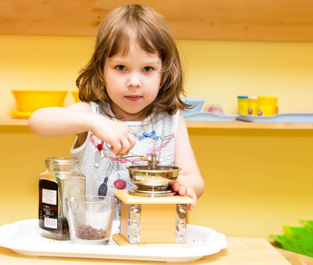 A cute little girl in the kitchen uses a hand grinder