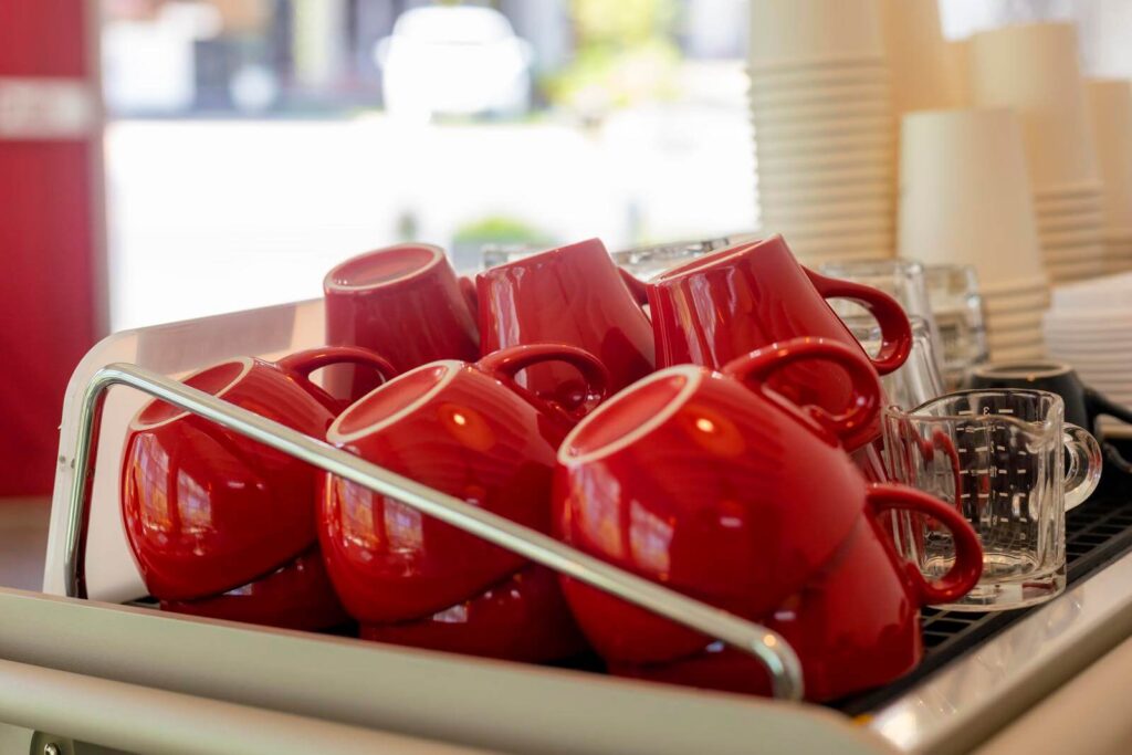 Lots of ceramic red coffee cups on espresso machine shelf in coffee shop