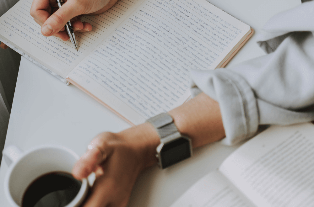 woman writing while holding a cup of coffee