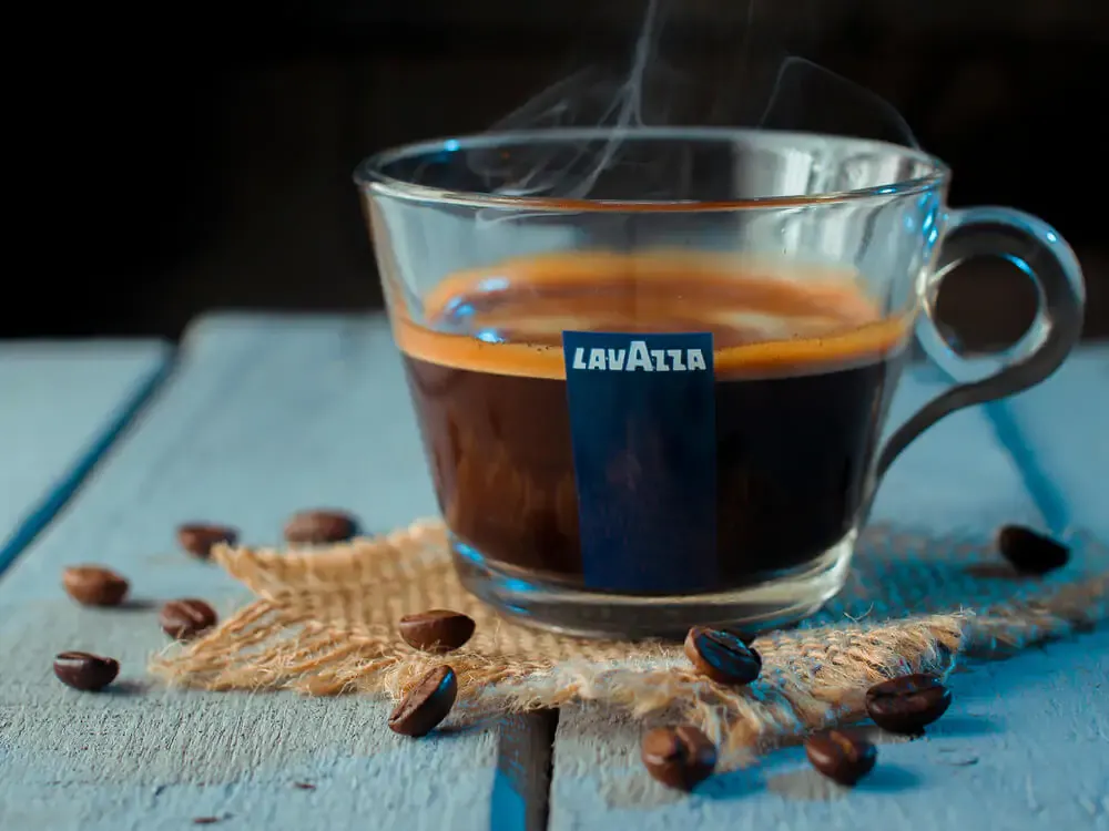 An espresso Lavazza glass cup with coffee beans around