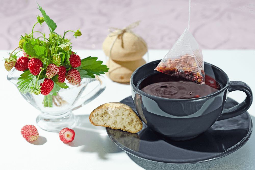 Cup of hot berry tea in bags, cookies, and a bouquet of wild berries