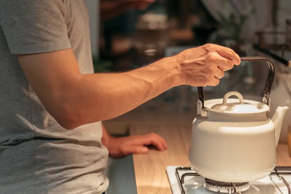 Man holding a stove kettle on top of gas stove