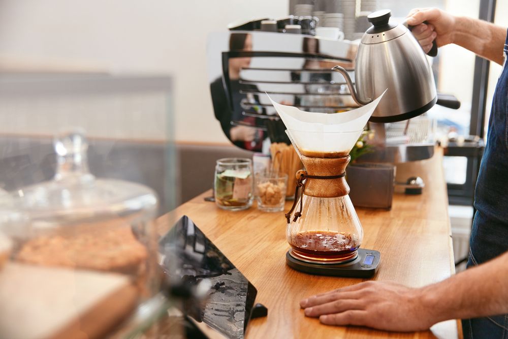 Barista holding a hot kettle while using pour-over coffee maker