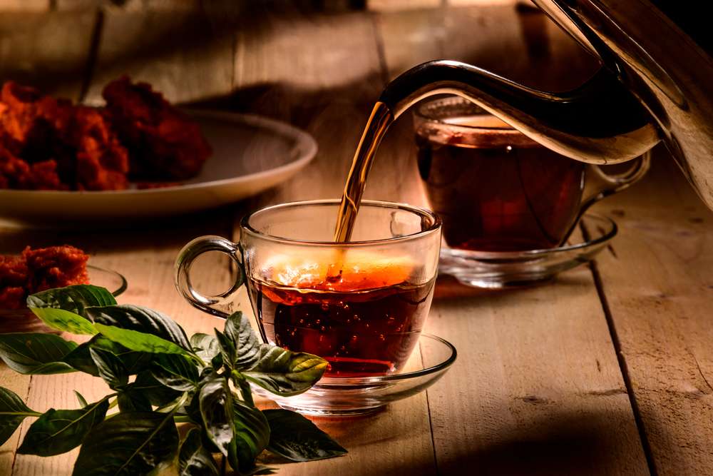 Hot steaming black tea in a cup on a rustic background