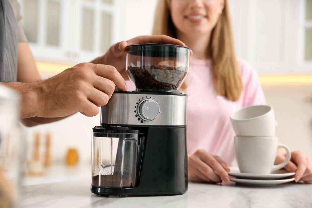 Couple together in kitchen. Man using electric coffee grinder