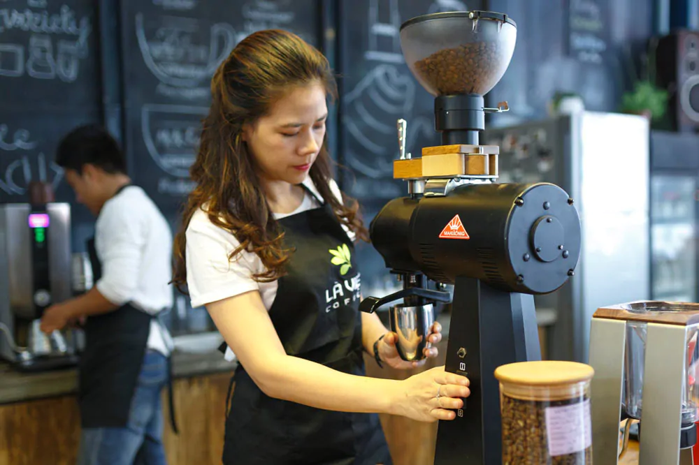 woman grinding coffee beans in an automatic coffee grinder