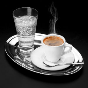 A cup of coffee on a table, with a glass of soda.