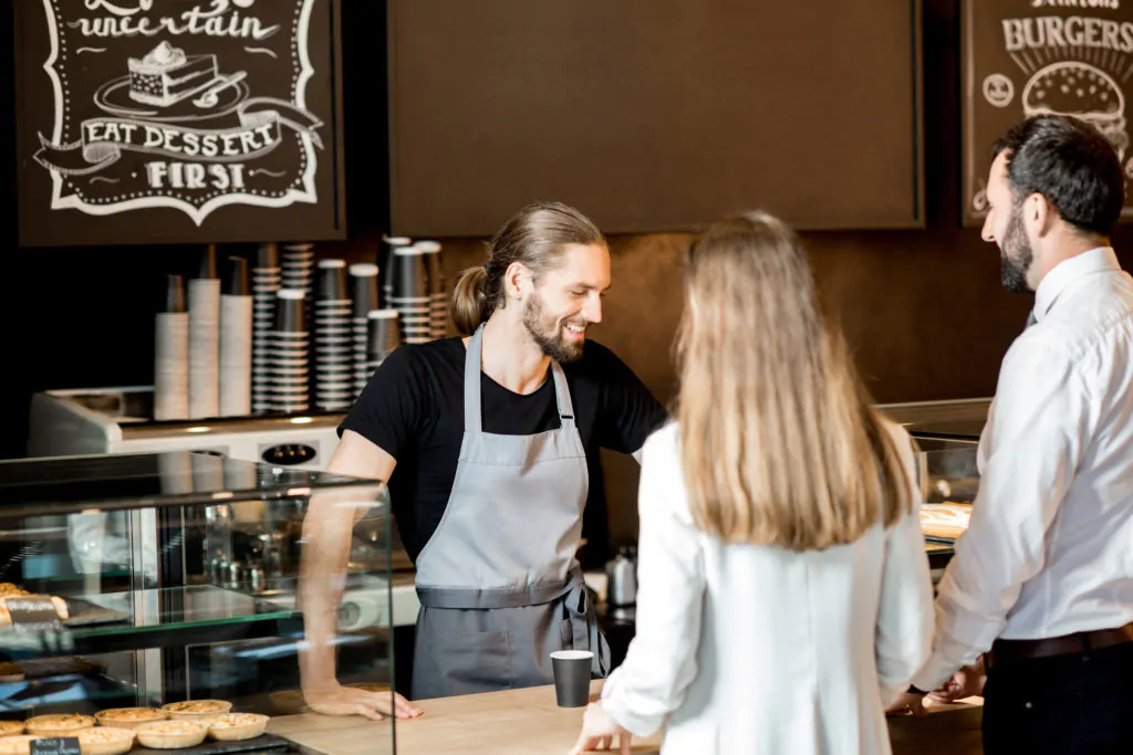 Young business couple buying coffee standing with handsome barista in the modern coffee shop