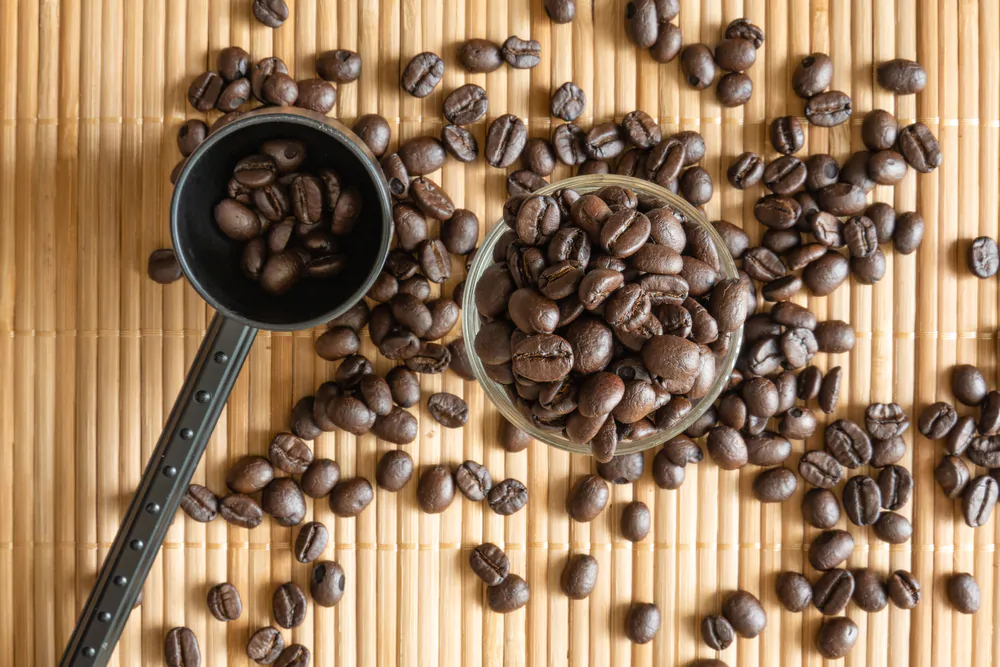 A cup of coffee beans and a measuring spoon on bamboo mat