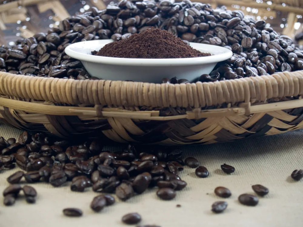 Dark roast ground coffee and beans in a bamboo basket