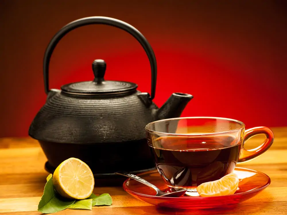 A kettle and a glass of black tea with a sliced lemon.