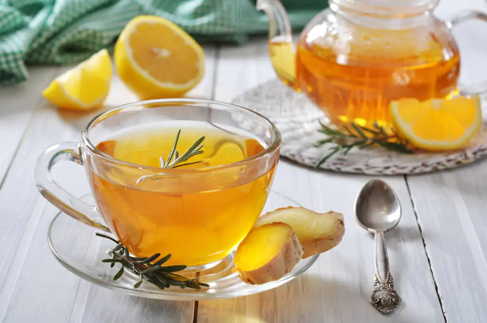 ginger tea in a cup and also in a kettle with a spoon and sliced lemons