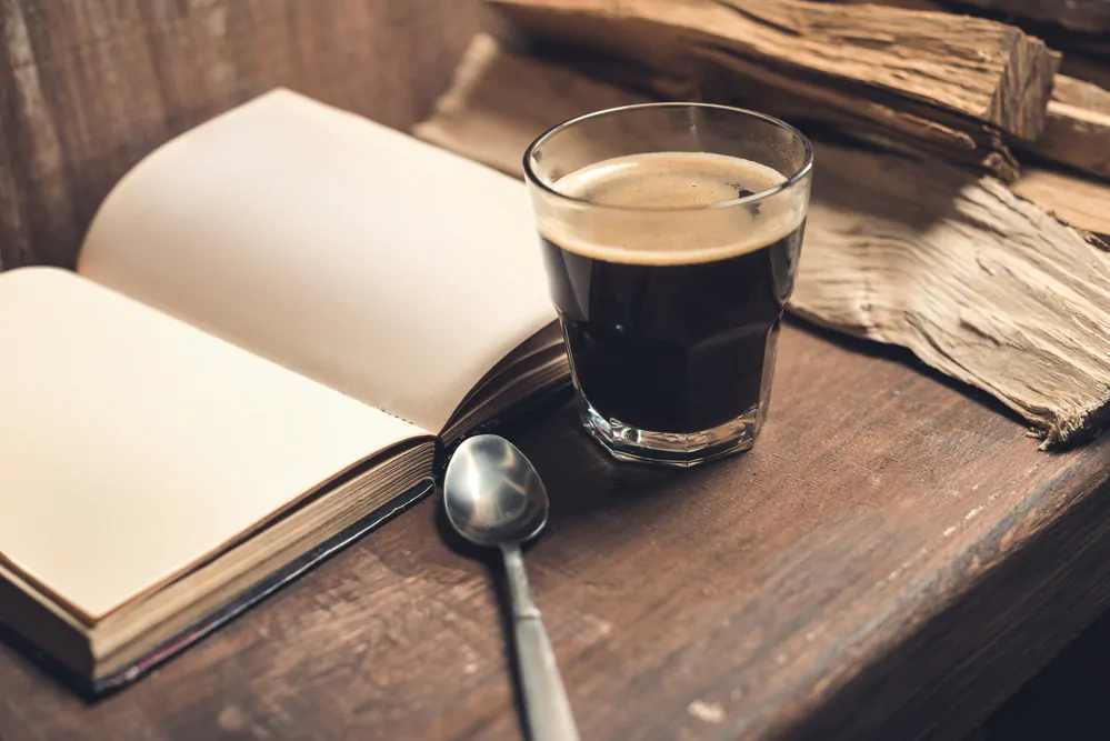 coffee on a table with a book and a spoon