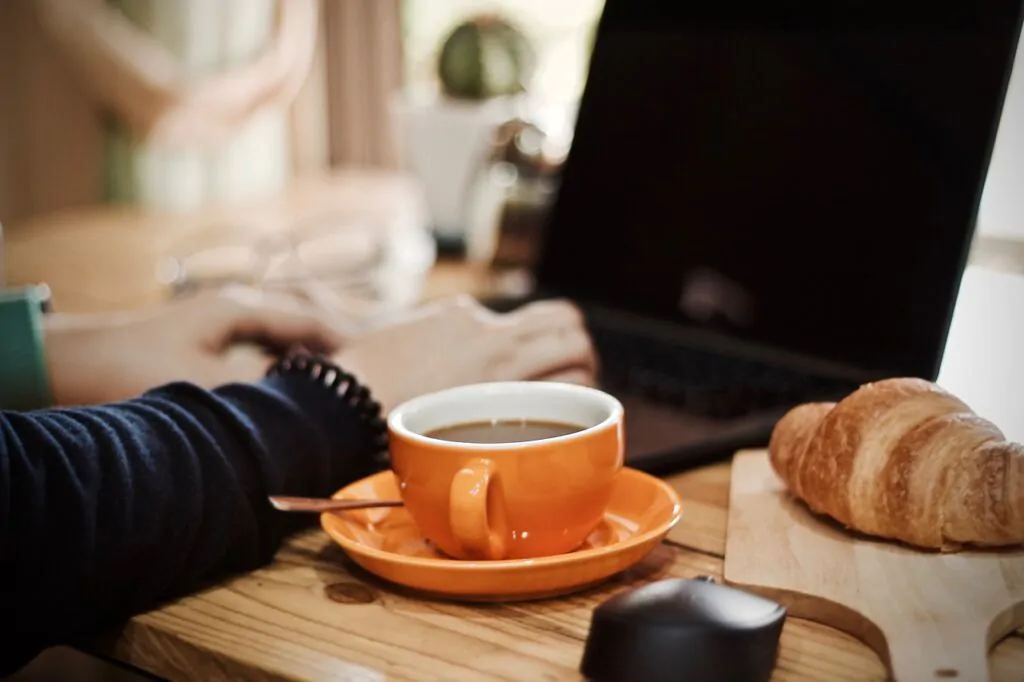 person using a laptop with a coffee and bread beside 