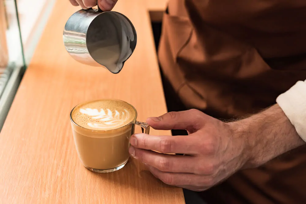 a hand pouring a milk to a coffee