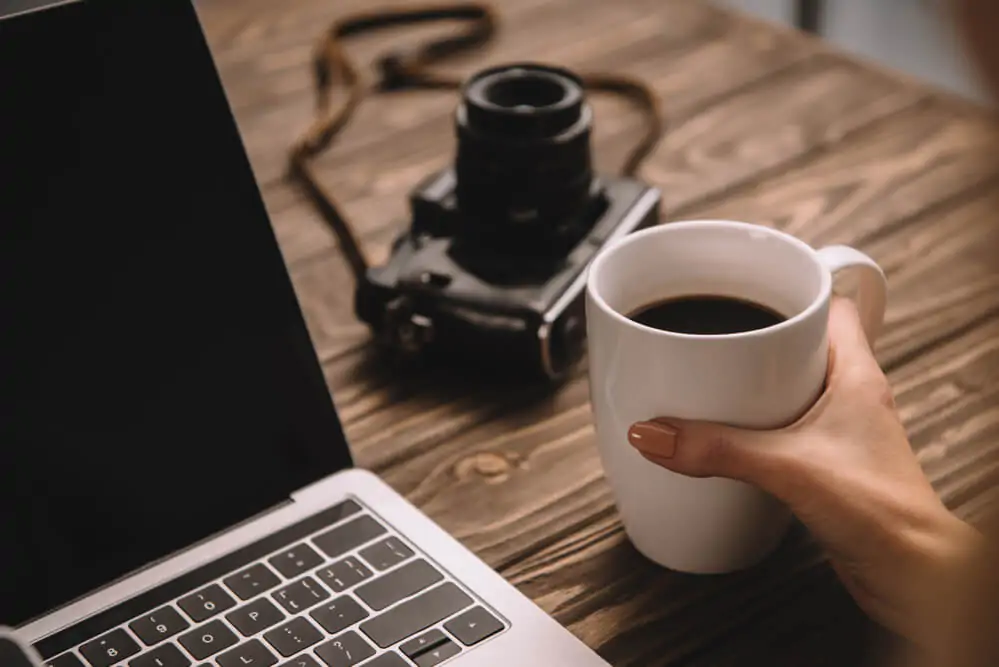holding a cup of coffee beside a laptop