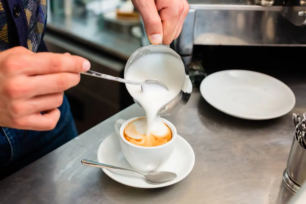 a man pouring milk in a cup of coffee