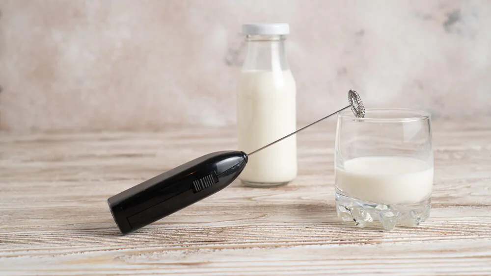 handheld milk frother placed at the mouth of a glass