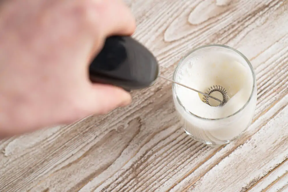 a man frothing milk inside a cup of glass