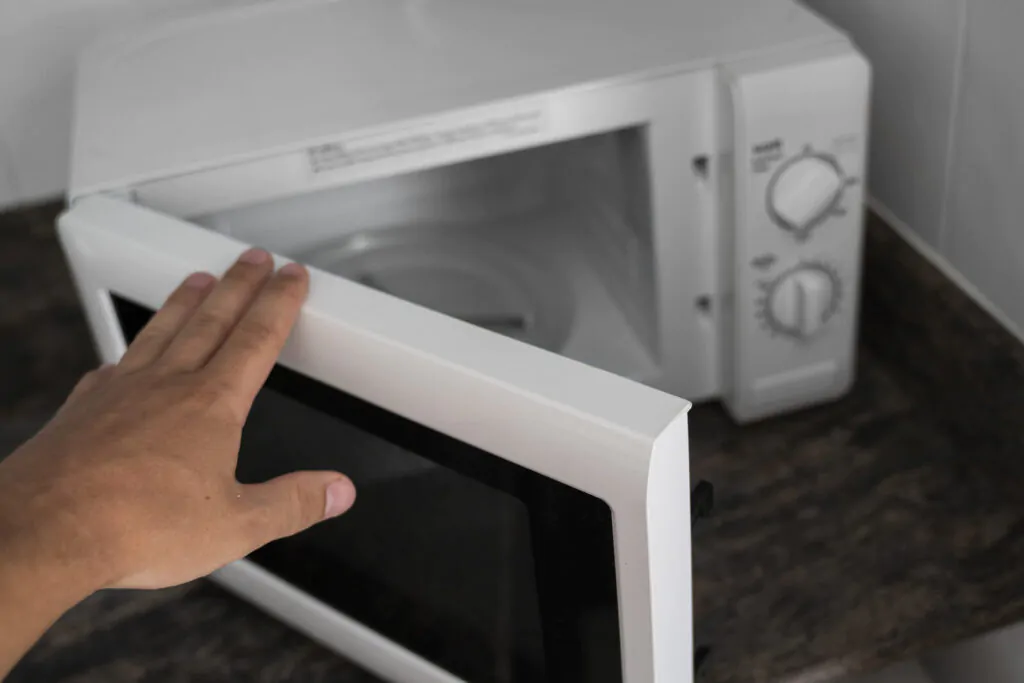 Man hand holdind a door of microwave in a kitchen for cooking or heating a dish