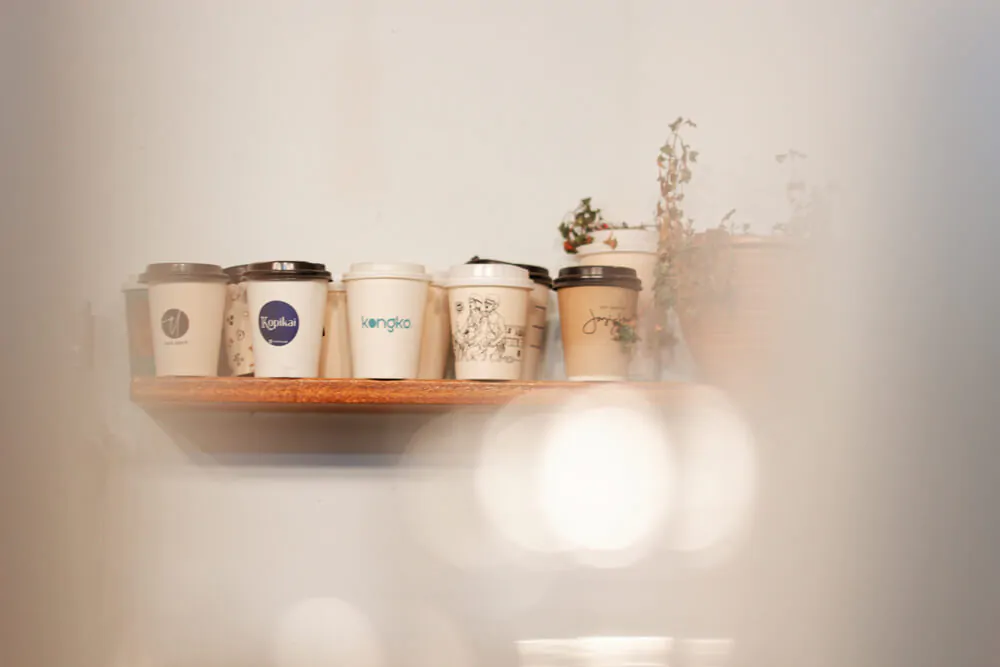 A collection of eco-friendly coffee cups from various local brands displayed on wall shelves