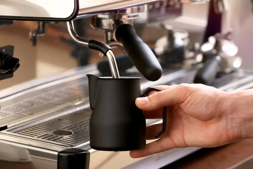 Barista whipping milk using the best milk frothing pitcher that is color black.