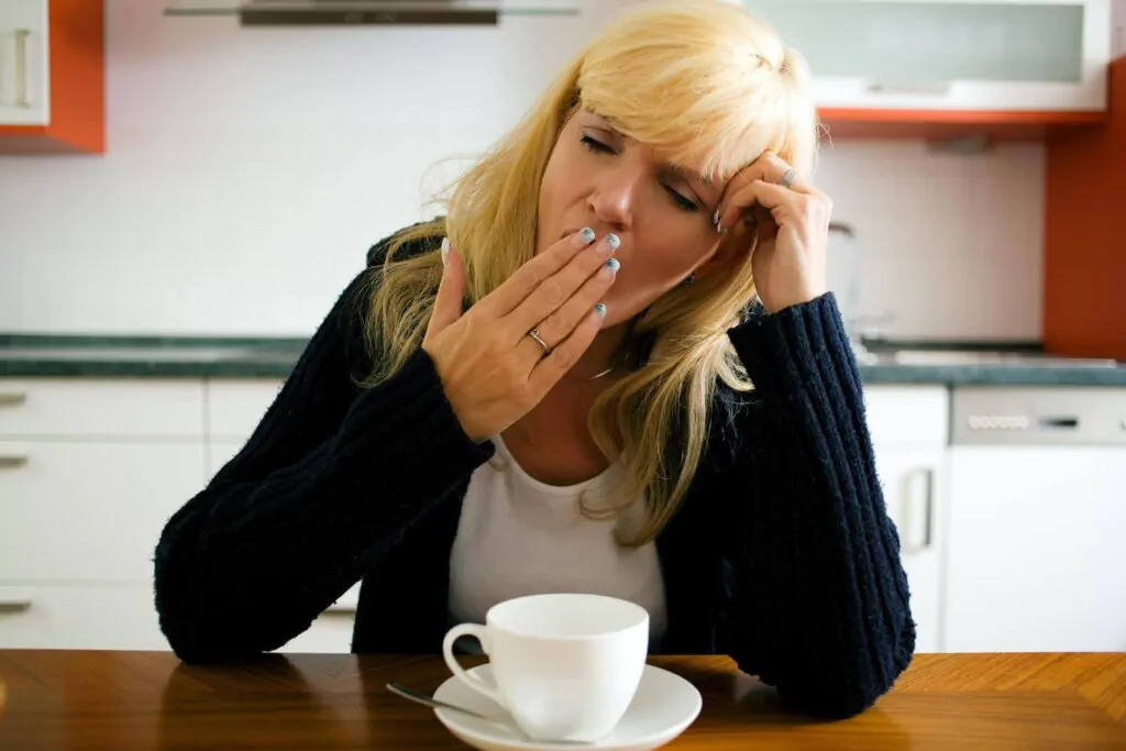Tired woman yawning in front of a mug full with coffee