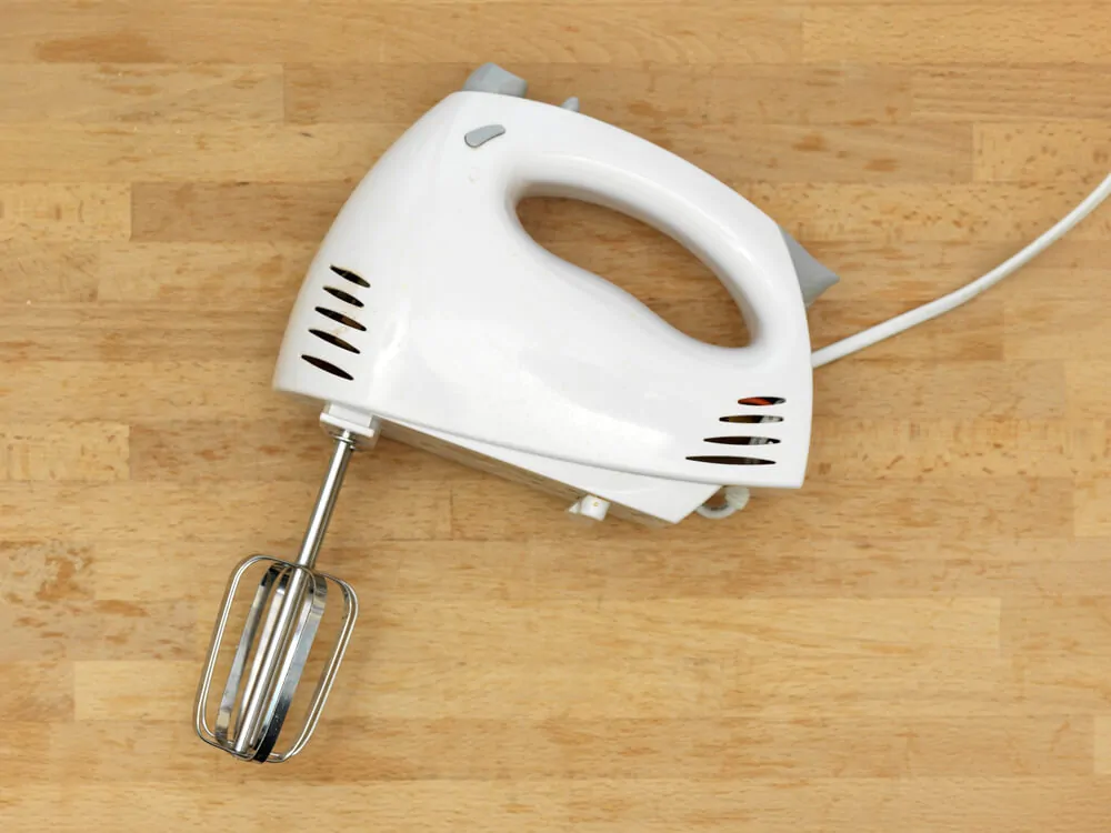A white electric hand mixer laid on top of a wooden table.