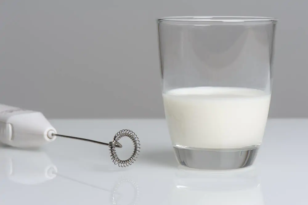 A milk frother and a milk in a clear glass cup.