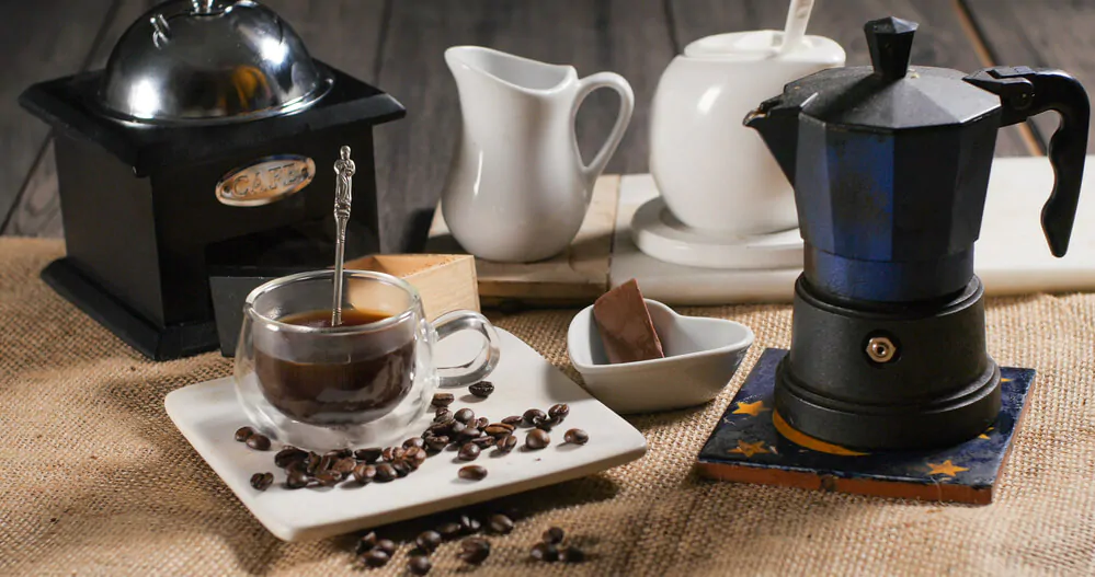 Moka pot on a wooden table with ceramics and a cup of coffee