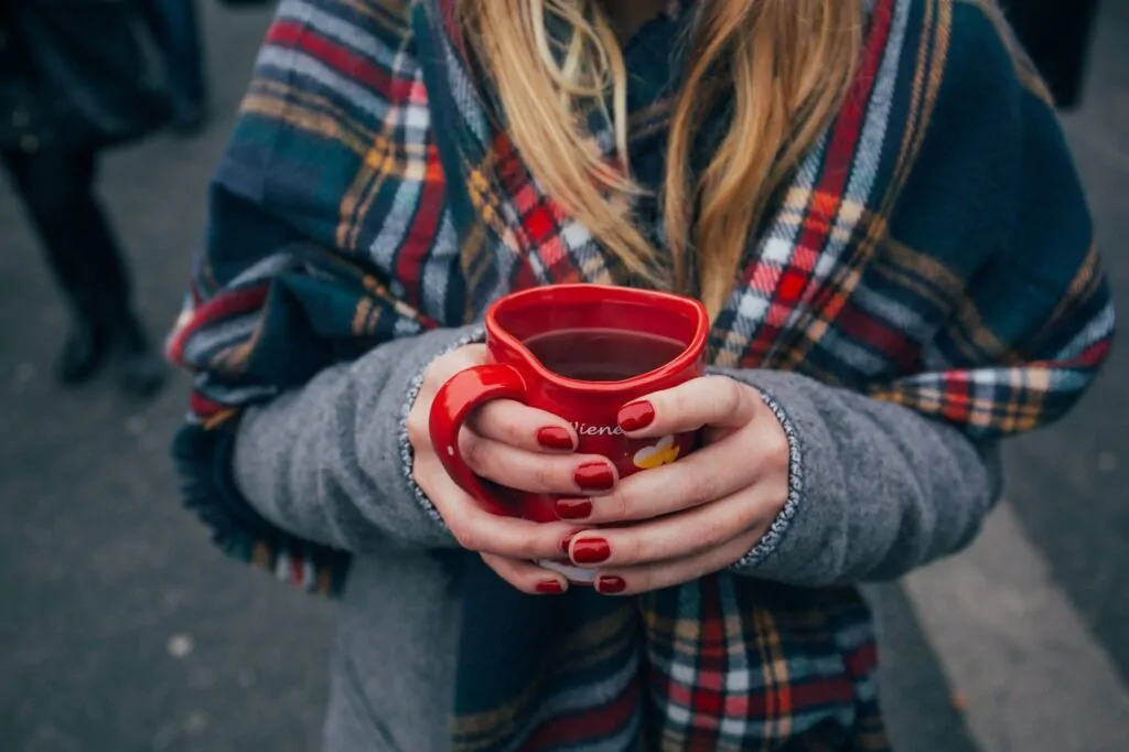 Woman holding a red hear-shape mug containing black coffee.