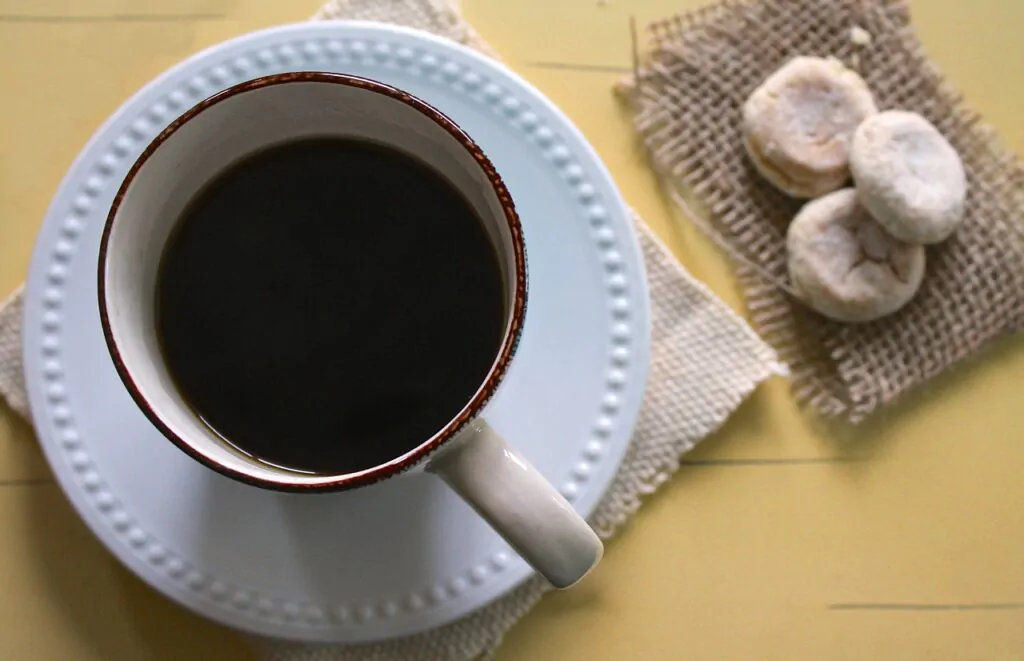 A cup of black coffee and three biscuits nearby.