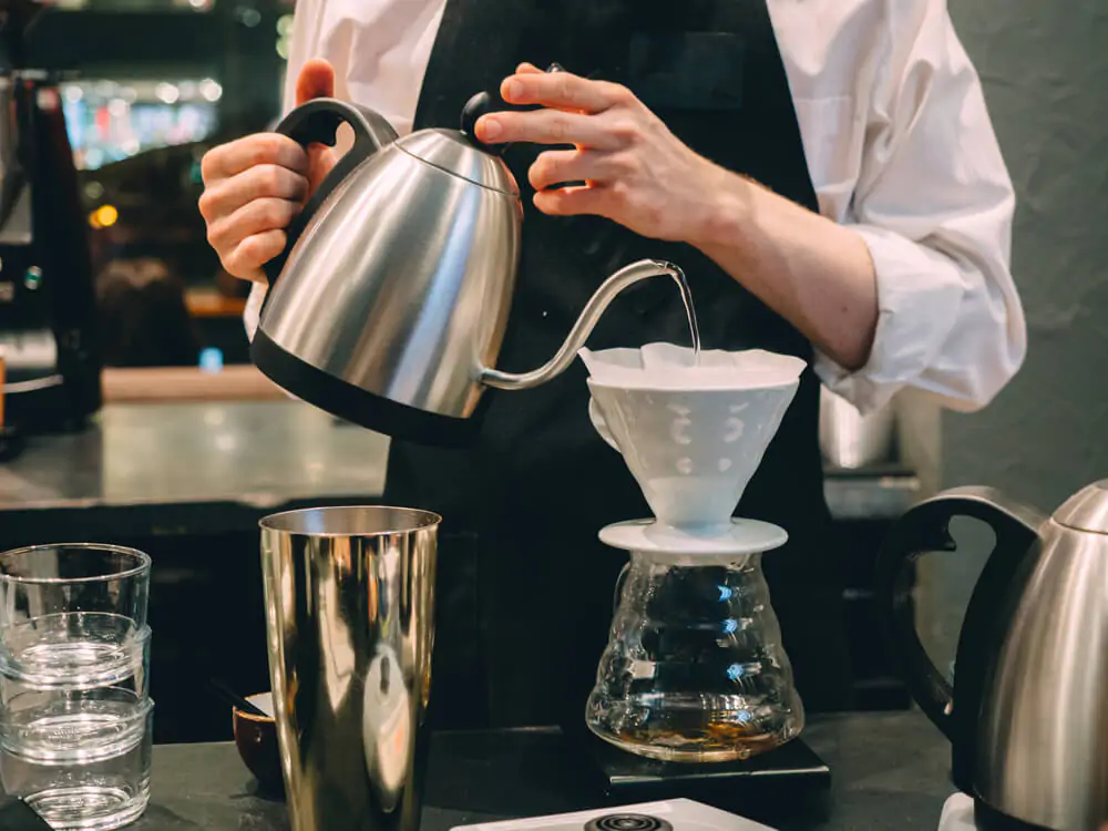 barista holding a kettle while pouring hot water to a chemex filter