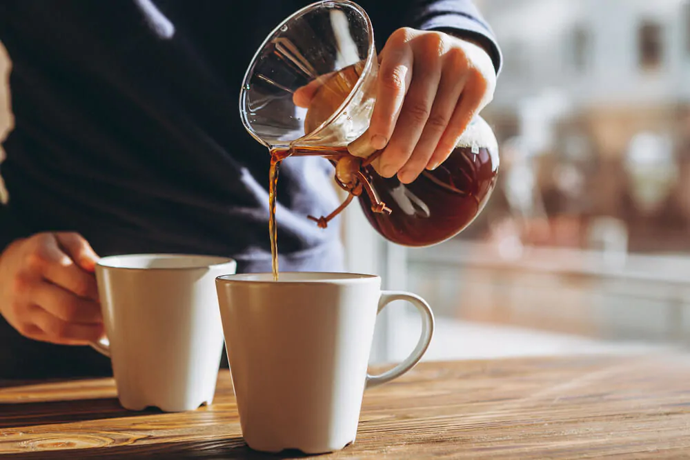 A person pouring coffee using chemex into a mug.