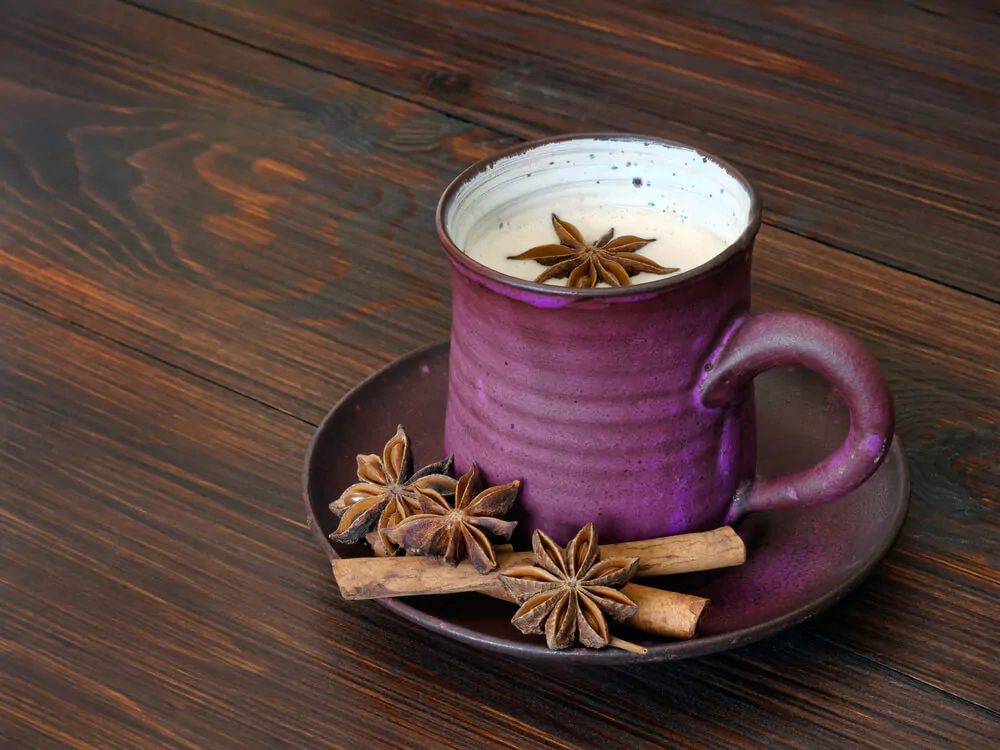 Herbal chai latte in a purple mug placed on a saucer with some raw spices.