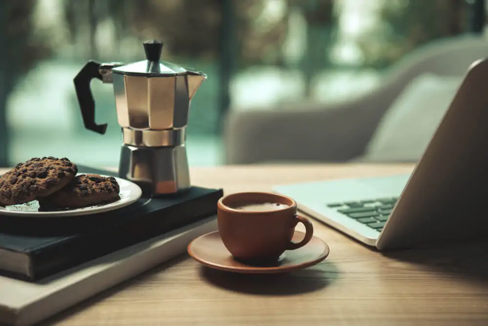 moka pot and a cup of coffee with laptop and cookies