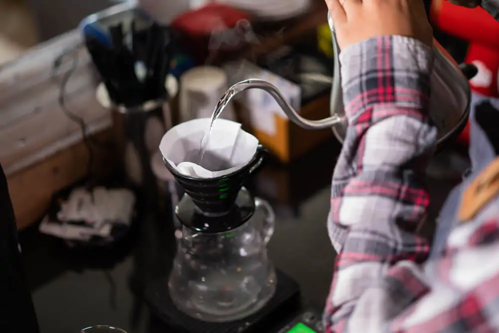 A person pouring water into a filter in a v60 coffee maker 