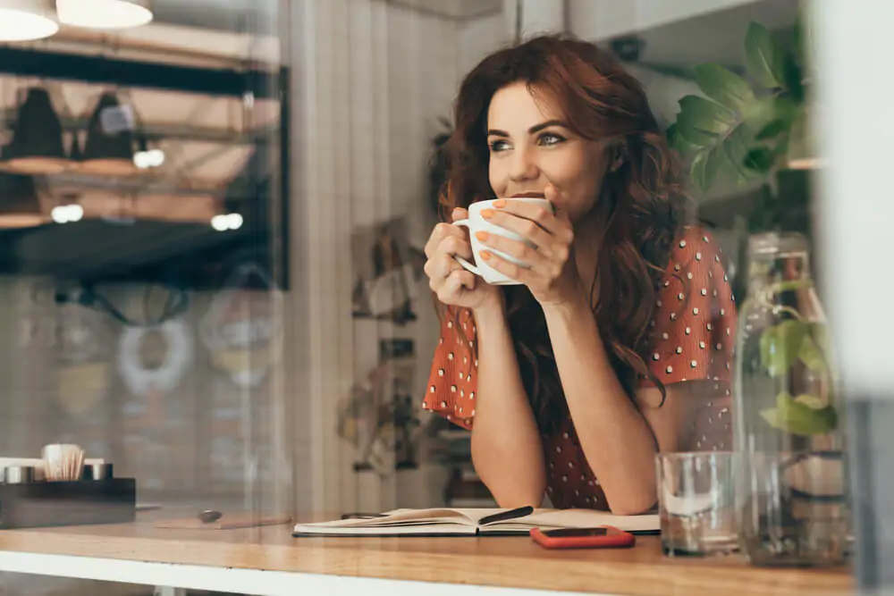 A woman with long curly hair drinking coffee. 