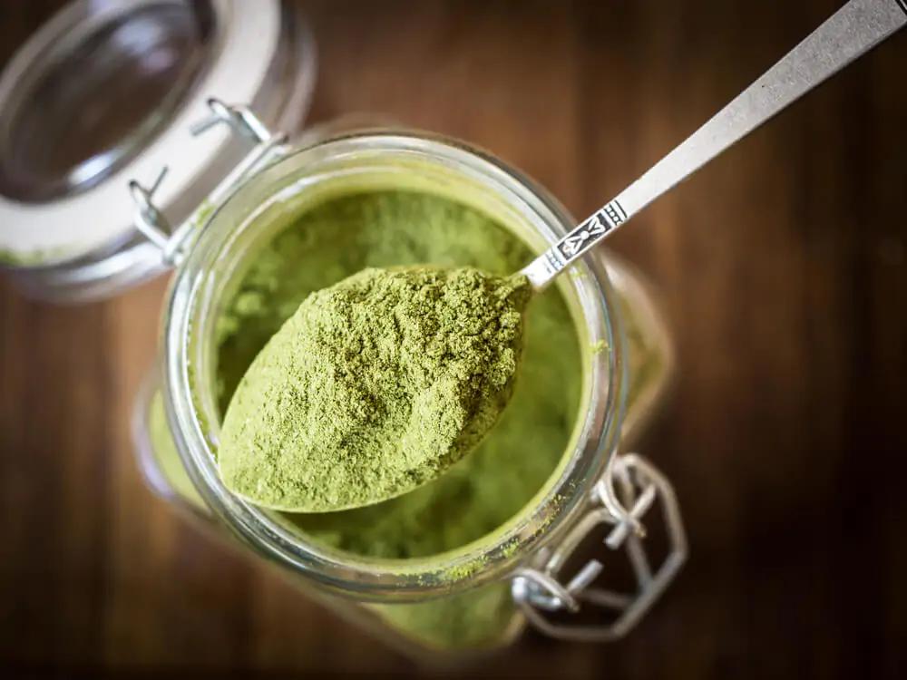 top view of a moringa powder in a glass jar with a spoonful of the powder
