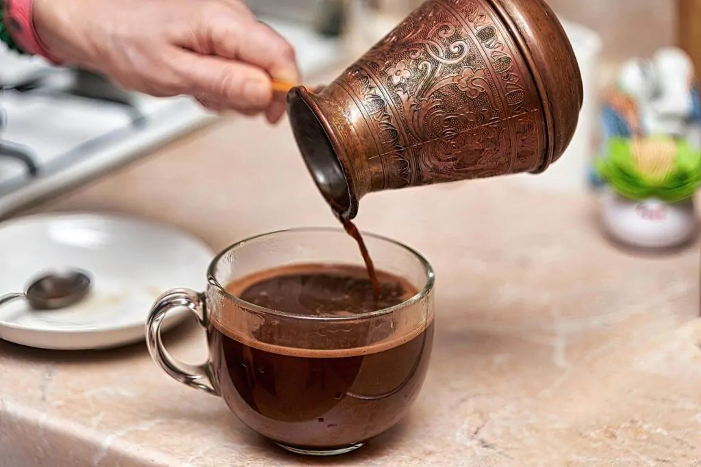 Coffee being poured down in a cup by Cezve pot