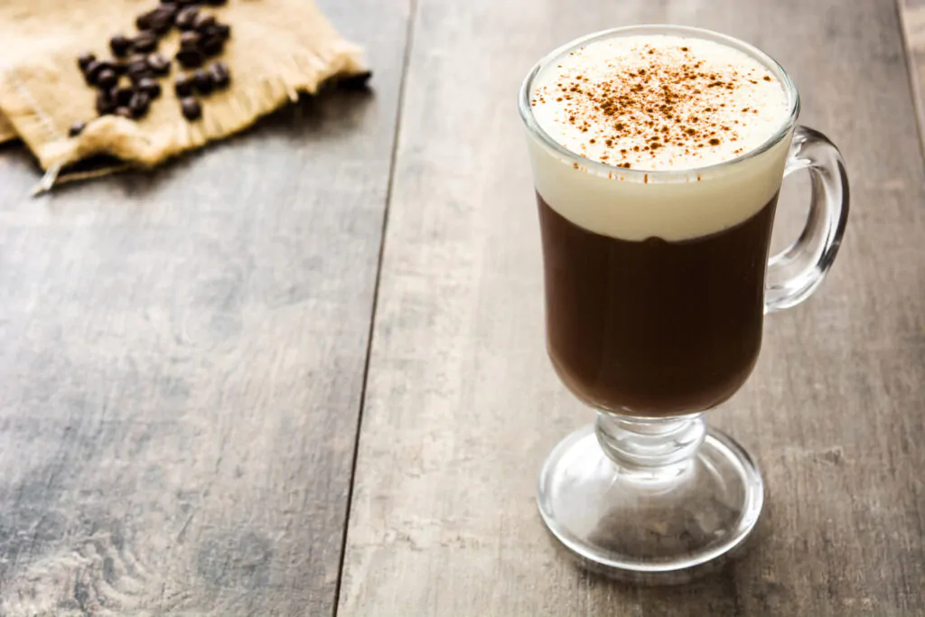 a cup of Irish coffee on a wooden table with coffee beans and a piece of cloth
