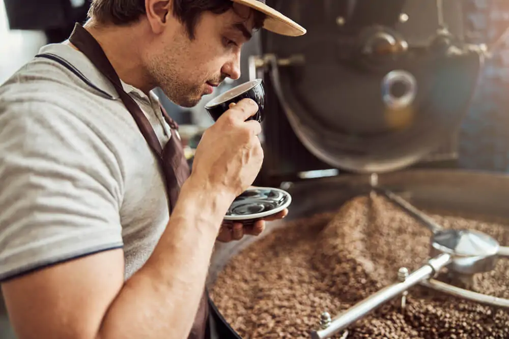 Handsome man smelling coffee near a coffee roasting machine