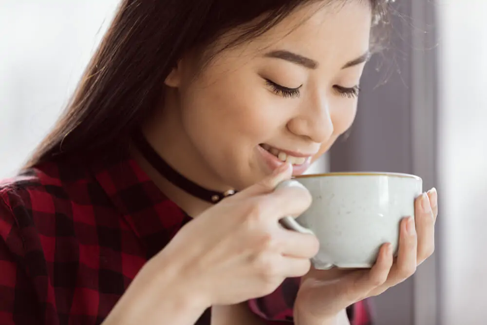 woman smiling while going to drinking her cup of coffee