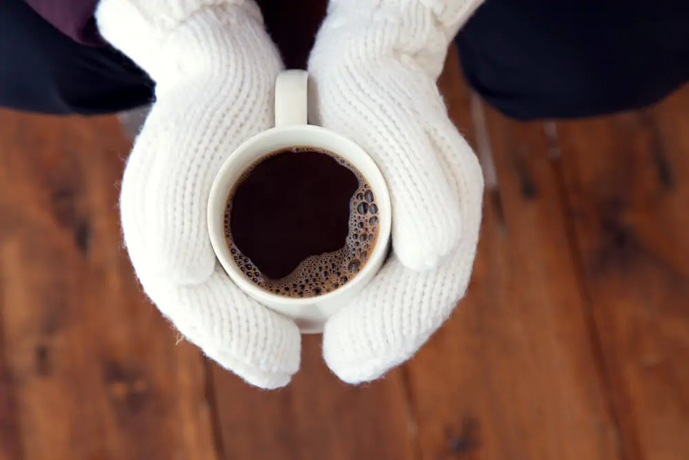 woman having gloves while holding a cup of coffee
