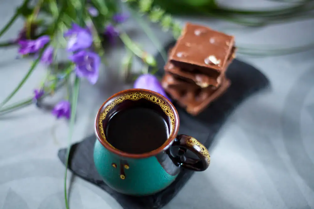 a ceramic mug with coffee and a chocolate biscuit